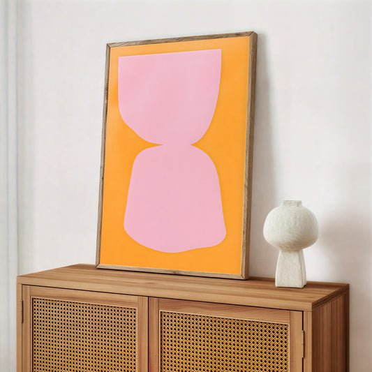 Framed abstract art with pink shape on orange background above a wooden cabinet.