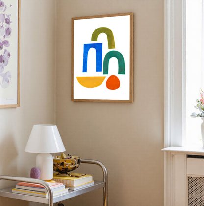 Colorful abstract art piece on a beige wall with a lamp and books on a table.