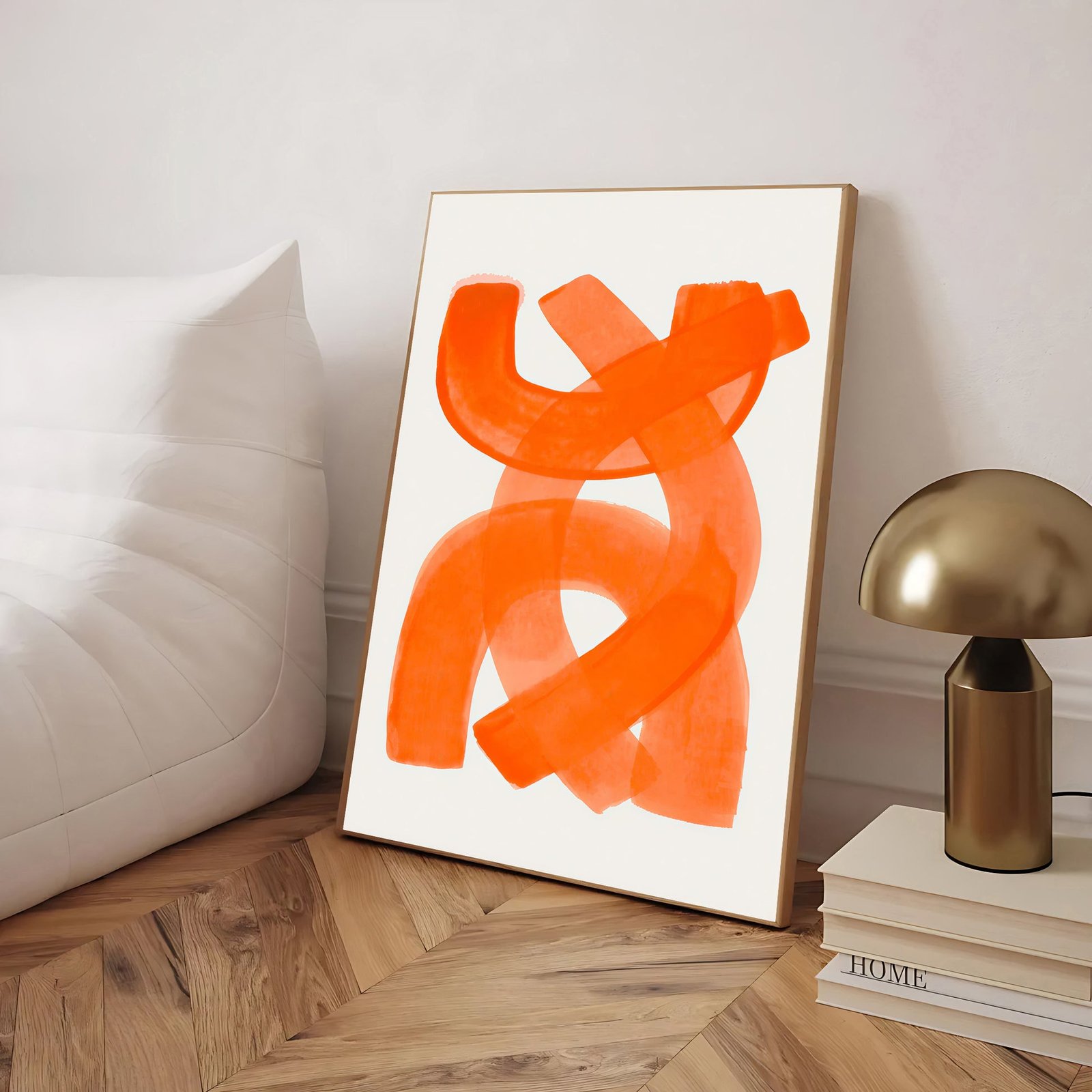 Orange abstract art piece on a white wall next to a gold lamp and books.