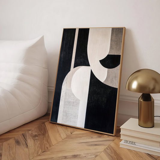 Abstract art piece on a wooden floor with a gold lamp and books in the background.