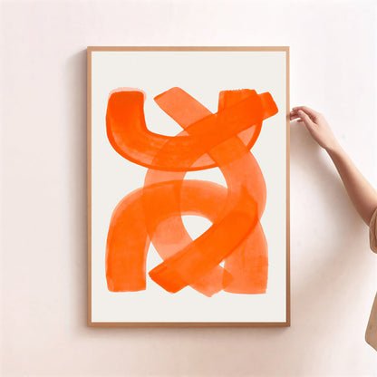 Framed abstract orange artwork on a white wall with a hand adjusting the frame.